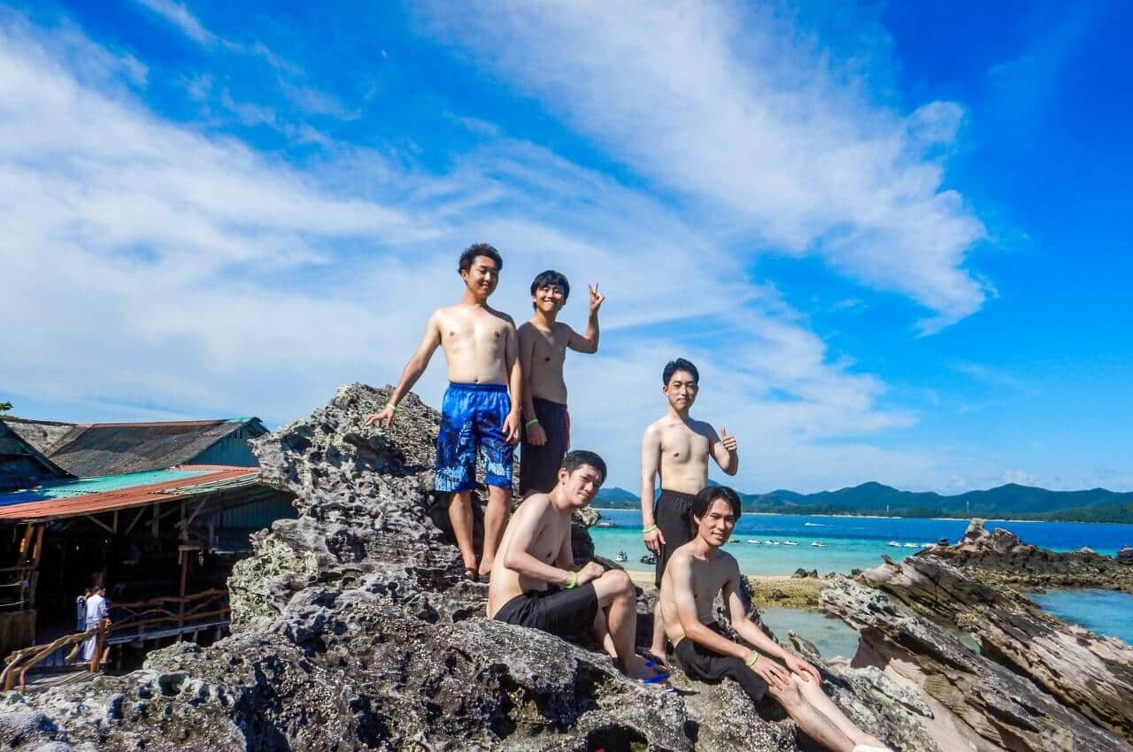 khai-island-five-guests-seaside-rocks カイ島の海沿いの岩場で並んで写真を撮る5名のお客様