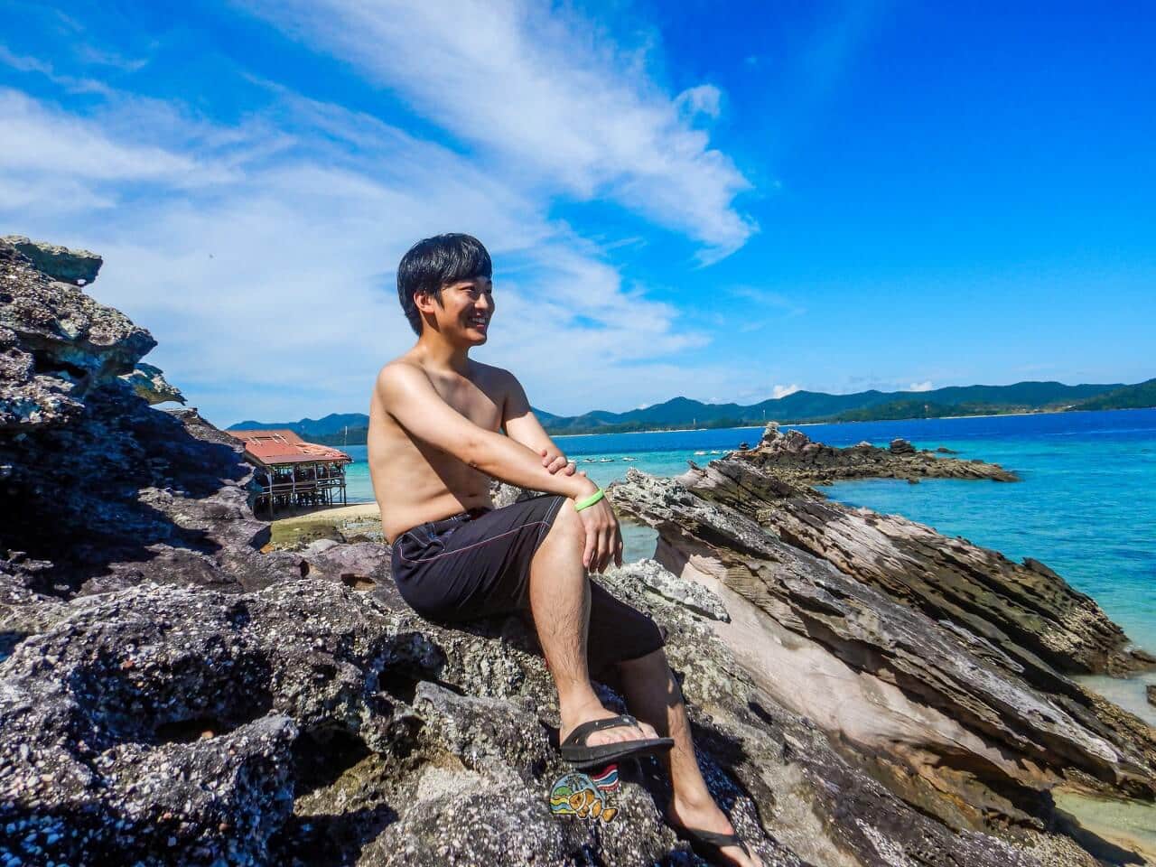 カイ島の岩場に座り青い海を眺めるお客様